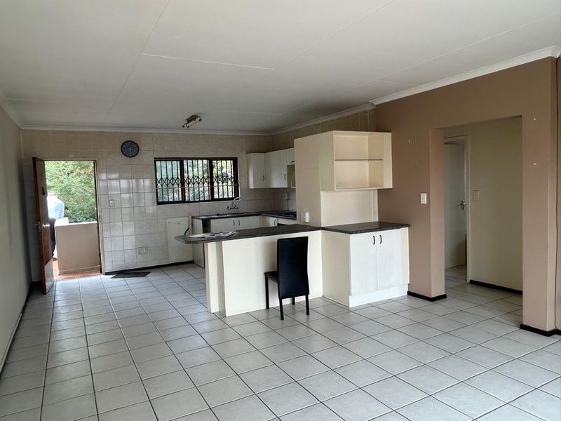 Open-plan kitchen and living area featuring tiled flooring, built-in cabinetry, a breakfast bar, and direct access to an outdoor space.