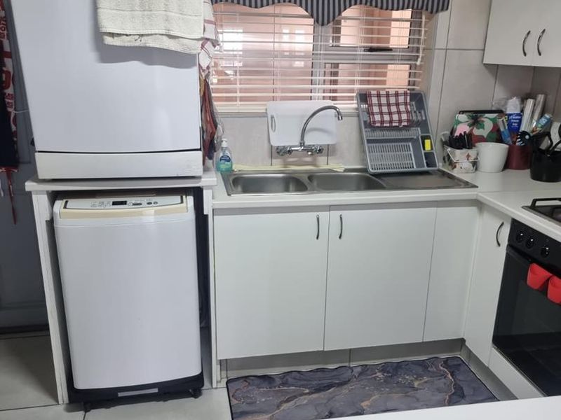 A functional kitchen featuring fitted white cabinetry, a double sink with mixer tap, built-in oven, hob, and tiled splashback finishes.