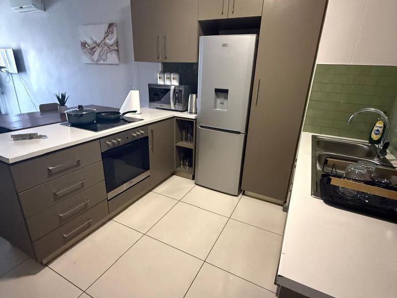 Modern kitchen featuring sleek taupe cabinetry, stone countertops, integrated appliances, and a stylish green subway tile backsplash with tiled flooring.