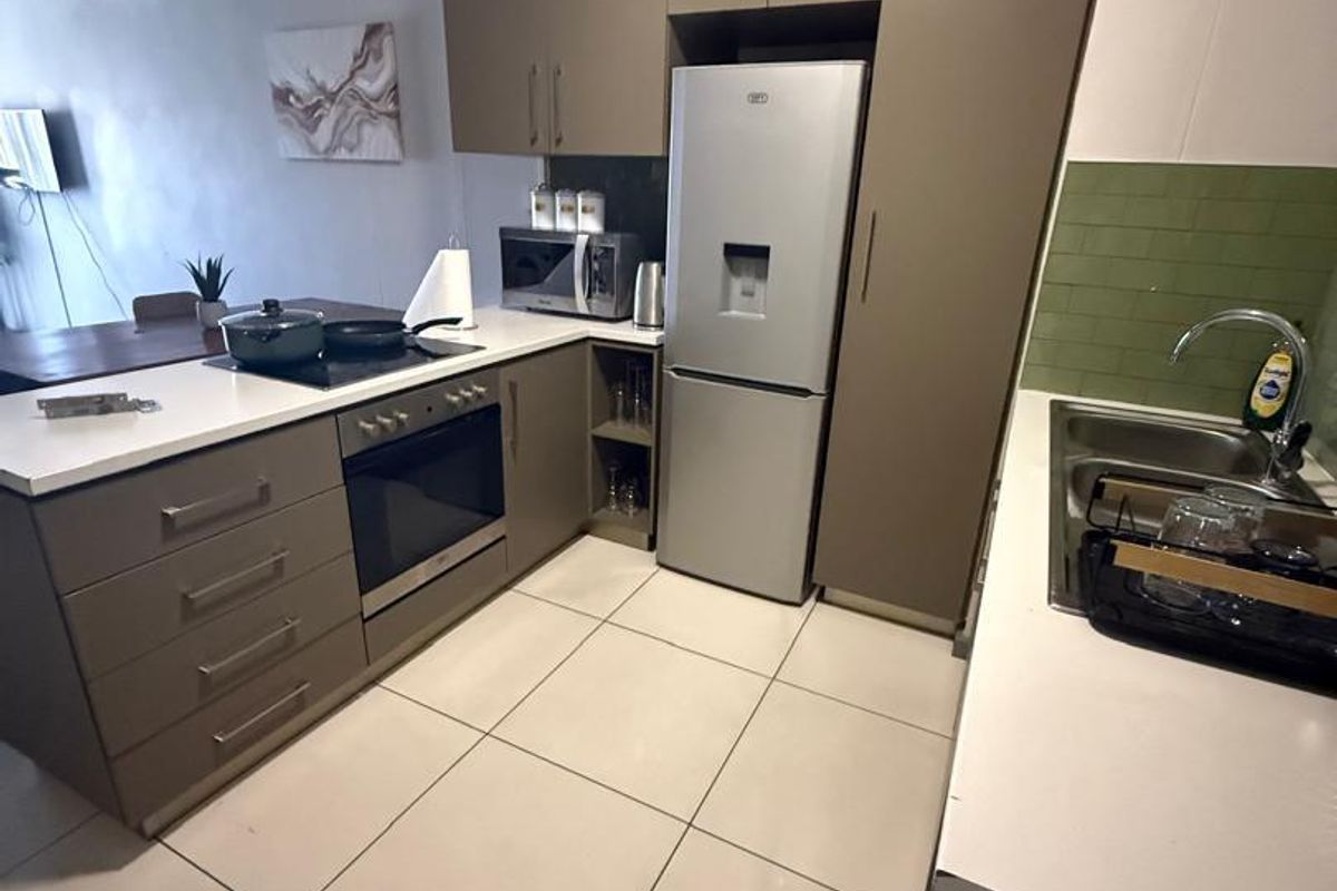 Modern kitchen featuring sleek taupe cabinetry, stone countertops, integrated appliances, and a stylish green subway tile backsplash with tiled flooring.