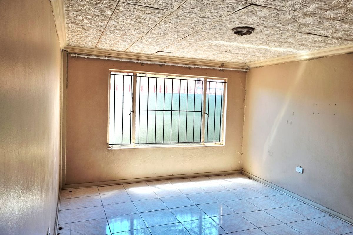 An empty living room featuring tiled flooring, decorative ceiling tiles, and a window fitted with security bars, offering a blank canvas for renovation.