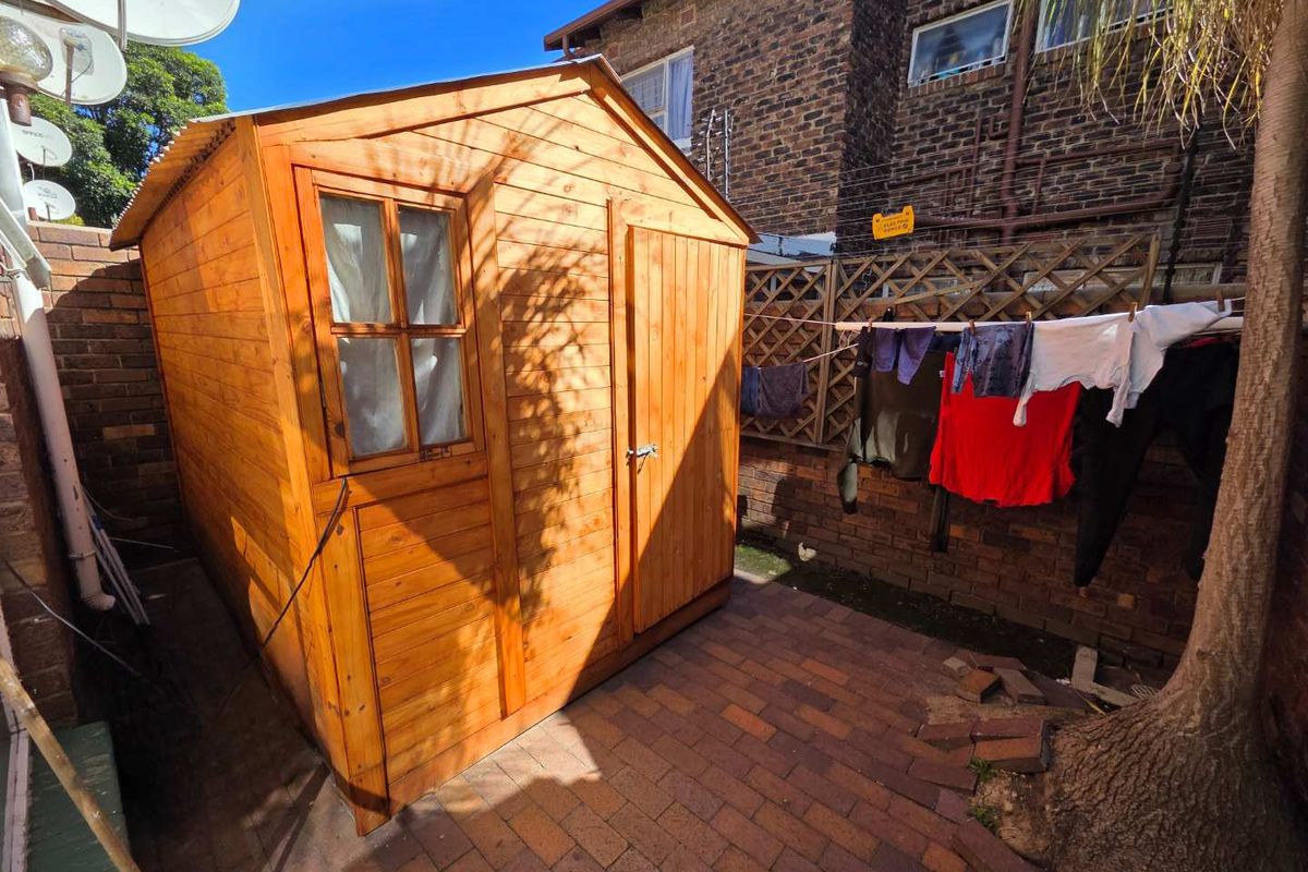 A rear courtyard area featuring a wooden storage shed, brick paving, and perimeter brick walling.