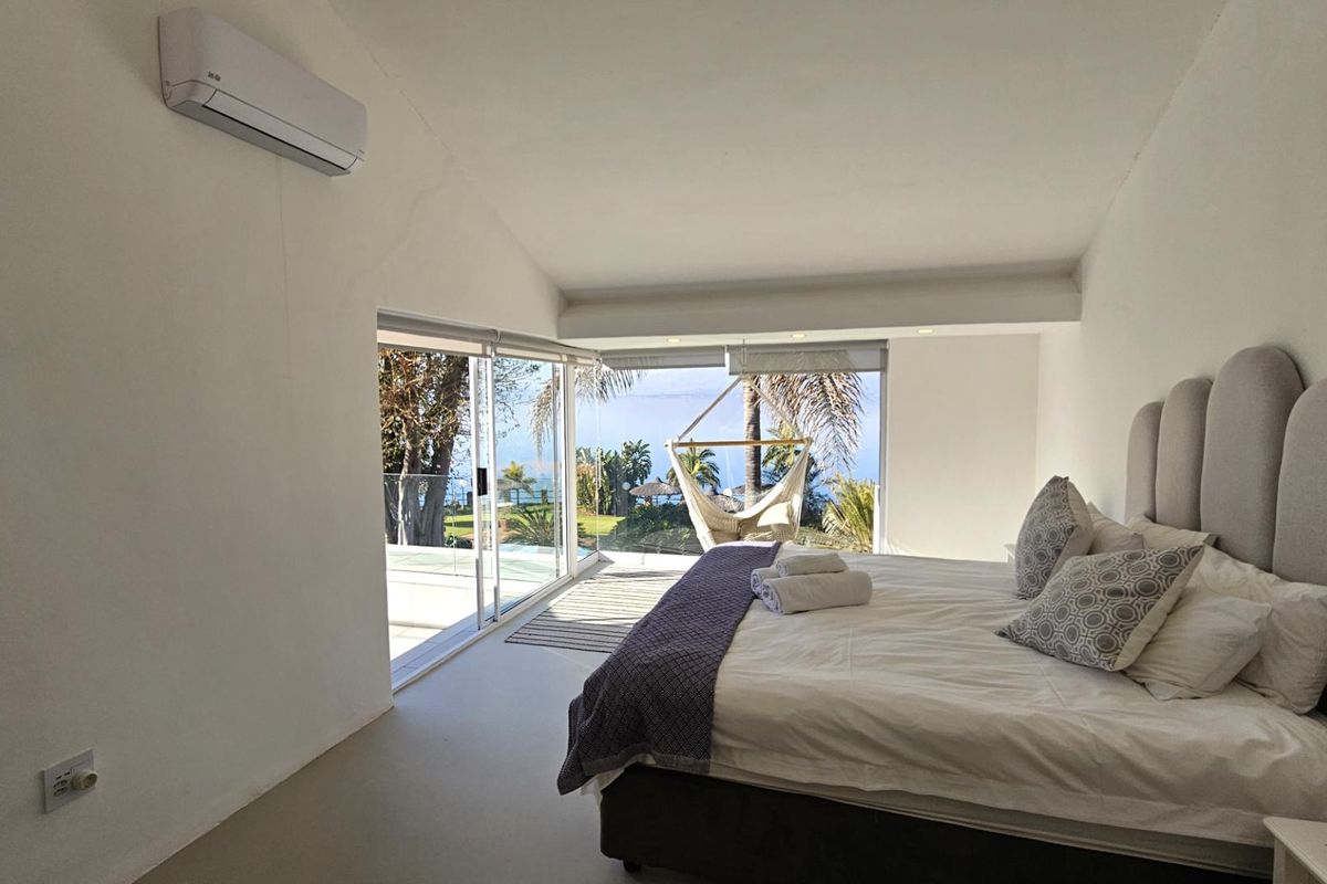 A bright, modern bedroom featuring large sliding glass doors that open to a scenic outdoor view, complemented by a wall-mounted air conditioning unit.