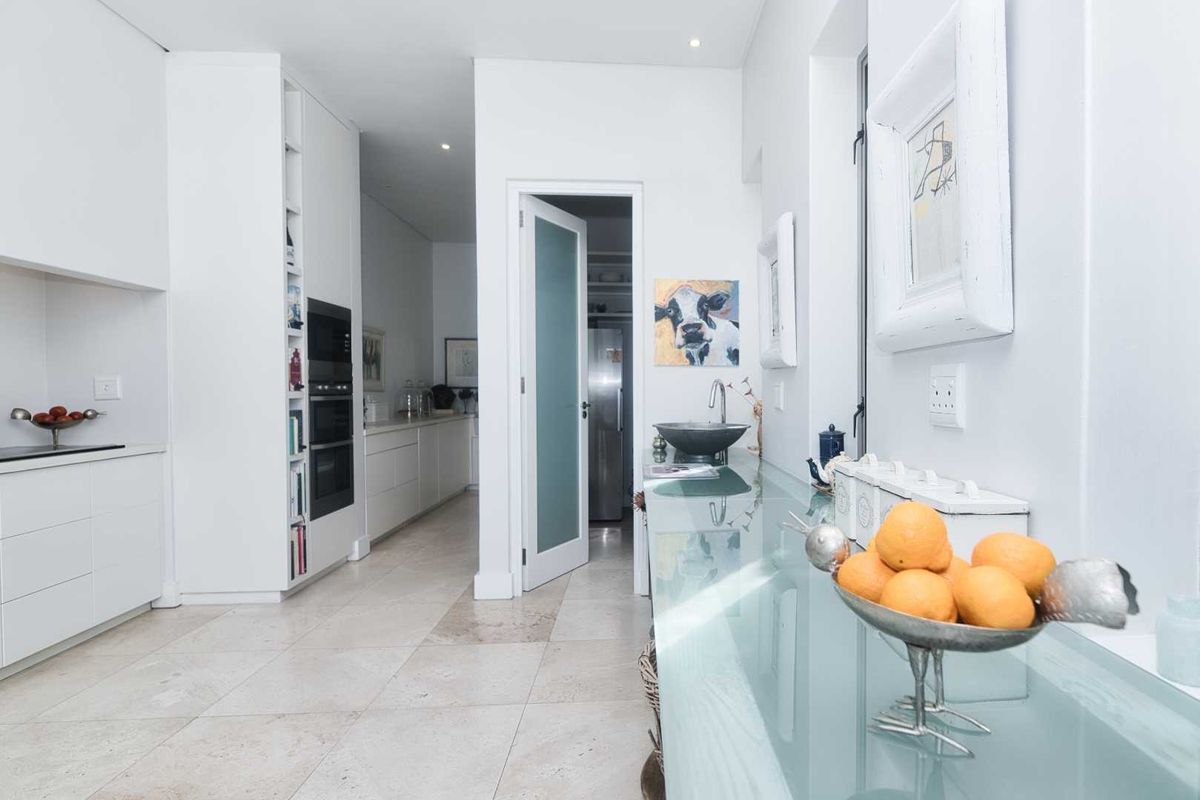 Modern kitchen featuring sleek white cabinetry, built-in ovens, stone flooring, and a glass-topped prep area with a secondary sink.
