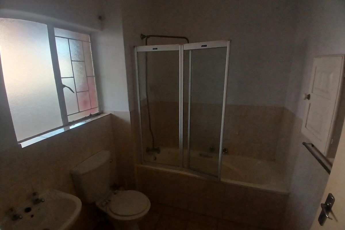 A dated bathroom featuring a bathtub with a shower screen, pedestal basin, and toilet, requiring cosmetic updates to modernize the space.