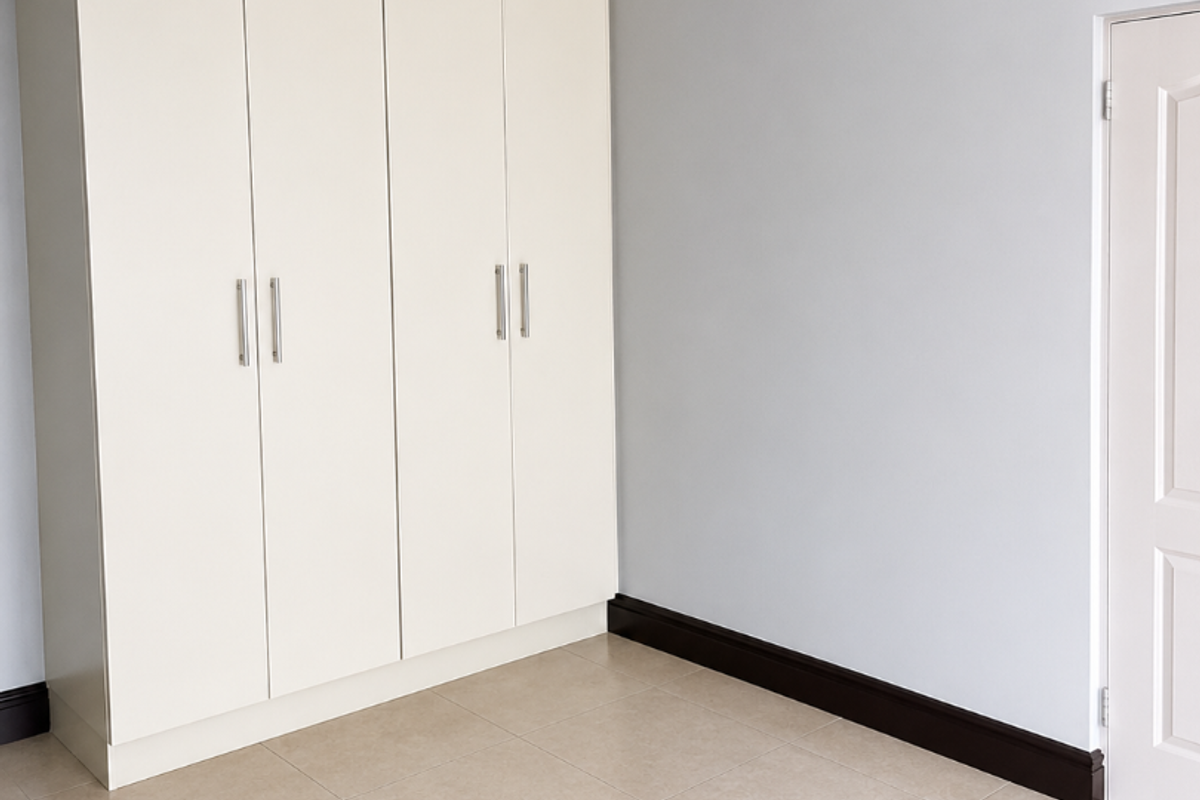 A clean, empty bedroom featuring neutral tiled flooring, built-in cupboards with modern handles, and crisp grey walls with white trim.