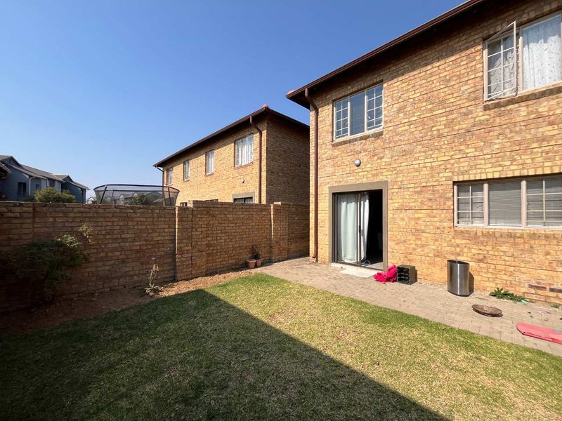 Rear view of a face brick house featuring a paved patio area, small lawn, and secure brick boundary wall.