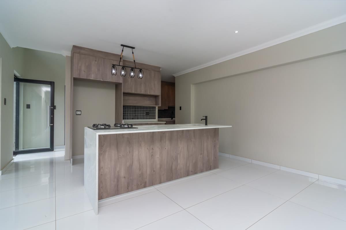 Modern kitchen featuring a central island with a gas hob, sleek wood-finish cabinetry, tiled backsplash, and polished white floor tiles in an open-plan layout.