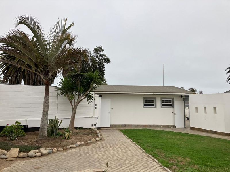 A well-maintained rear exterior view featuring a paved walkway, manicured lawn, and a clean white building facade with modern casement windows.