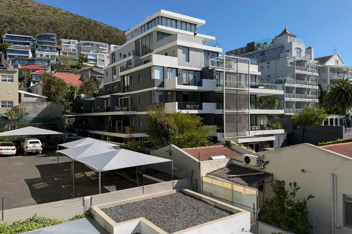 A modern multi-story apartment building featuring tiered balconies, contemporary facade finishes, and dedicated covered parking facilities in a hillside residential setting.