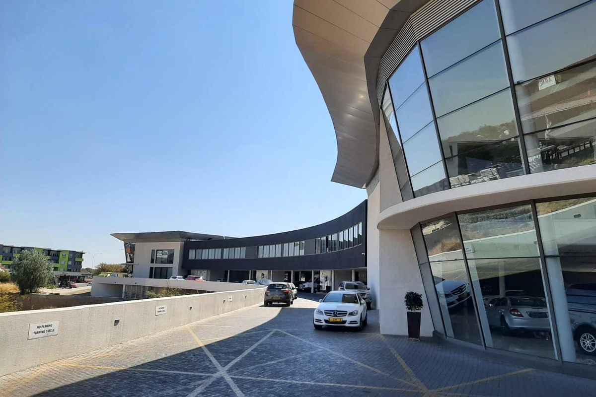 Modern commercial office building featuring a striking curved glass facade, contemporary architectural canopy, and a spacious paved driveway entrance.