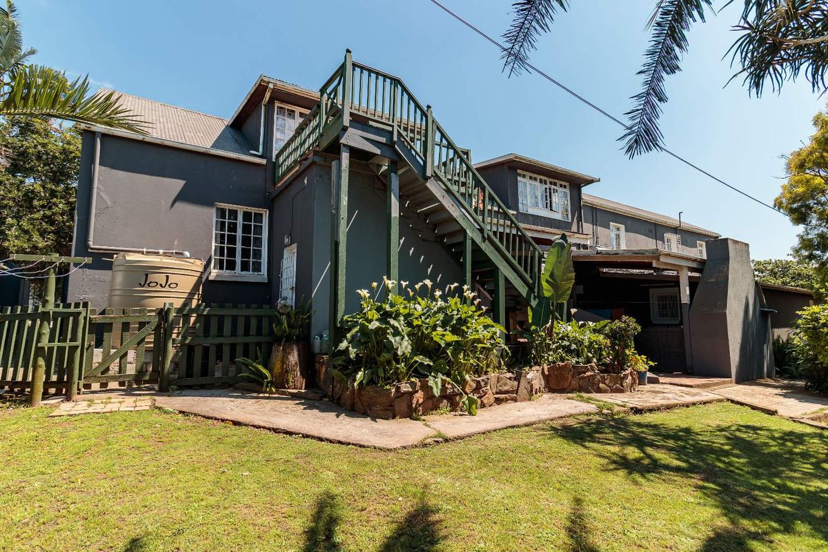 Rear exterior view of the property featuring a multi-level layout with an external staircase, paved garden paths, and a water storage tank.