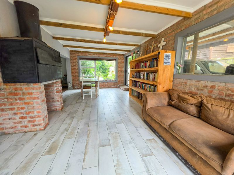 Spacious living area featuring exposed brick walls, timber ceiling beams, and a prominent wood-burning fireplace, creating a rustic and inviting atmosphere.
