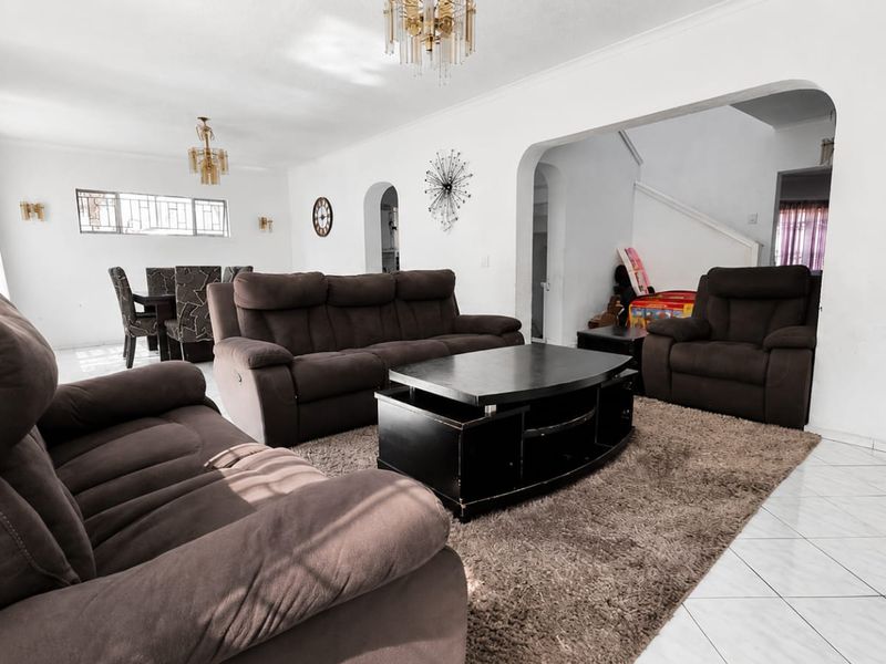Spacious open-plan living and dining area featuring tiled flooring, arched architectural details, and a staircase leading to the upper level.