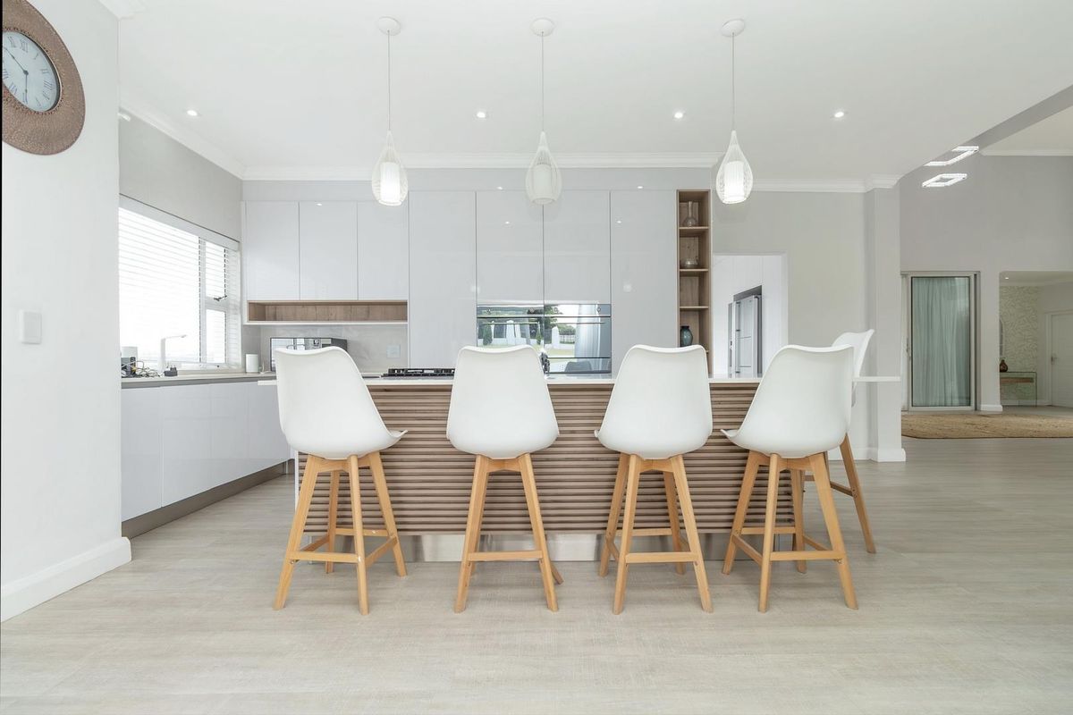 Modern open-plan kitchen featuring sleek white cabinetry, a central island with timber-slat detailing, integrated appliances, and contemporary pendant lighting.