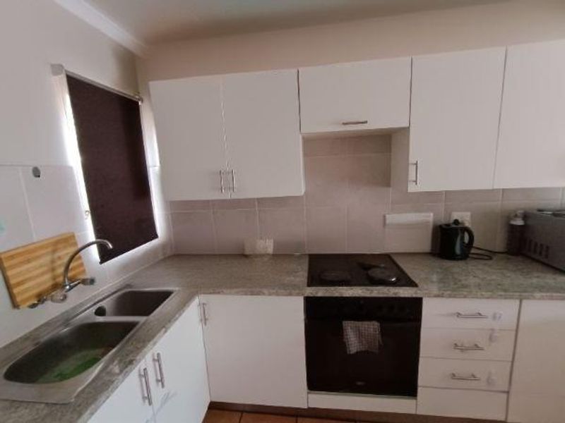 A functional kitchen featuring white cabinetry, laminate countertops, a stainless steel double sink, and a built-in oven with an electric hob.