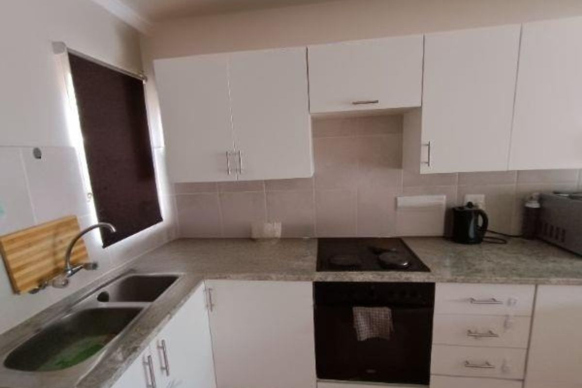 A functional kitchen featuring white cabinetry, laminate countertops, a stainless steel double sink, and a built-in oven with an electric hob.