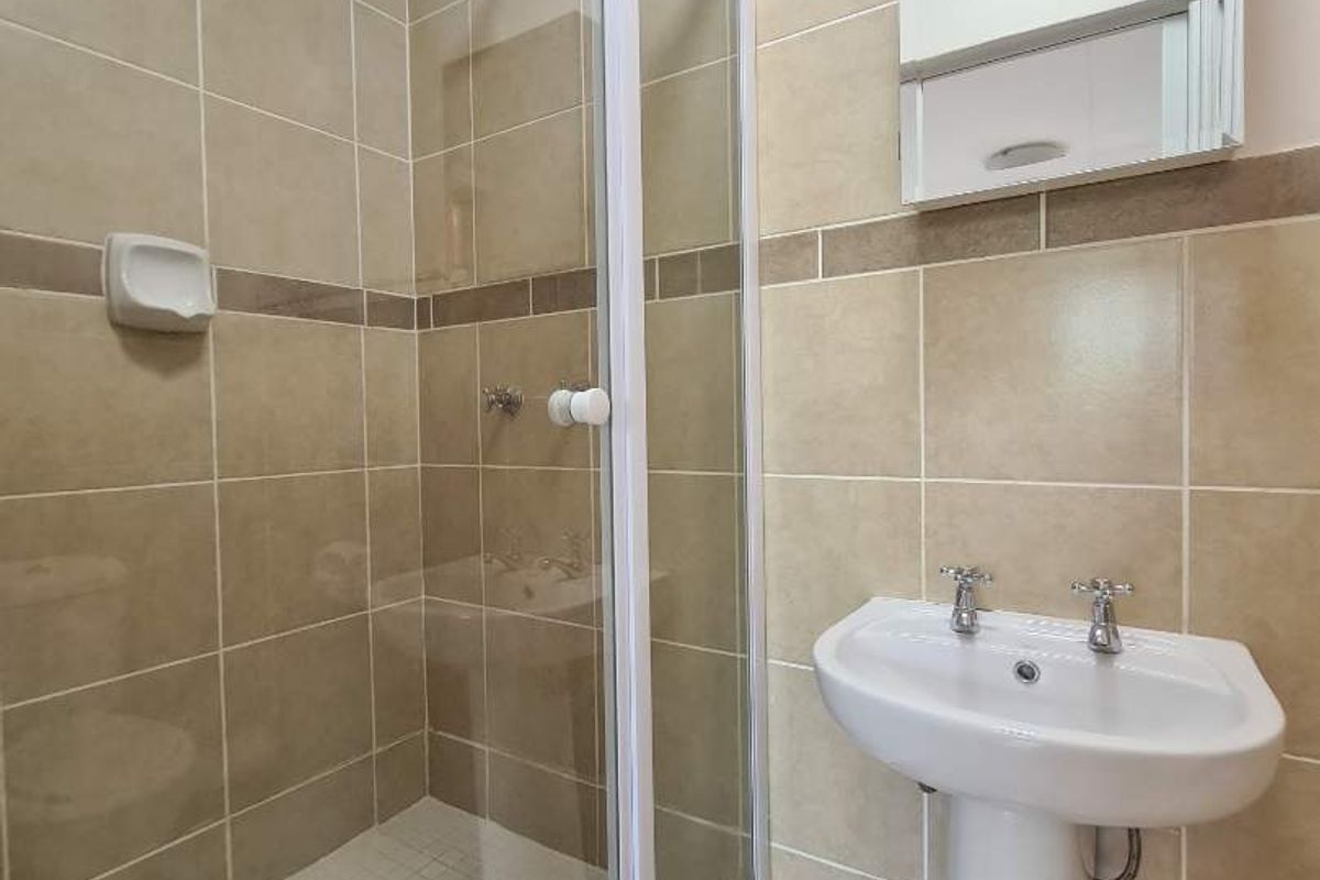 A functional bathroom featuring a glass-enclosed shower, pedestal basin, and wall-mounted medicine cabinet with neutral ceramic tiling throughout.