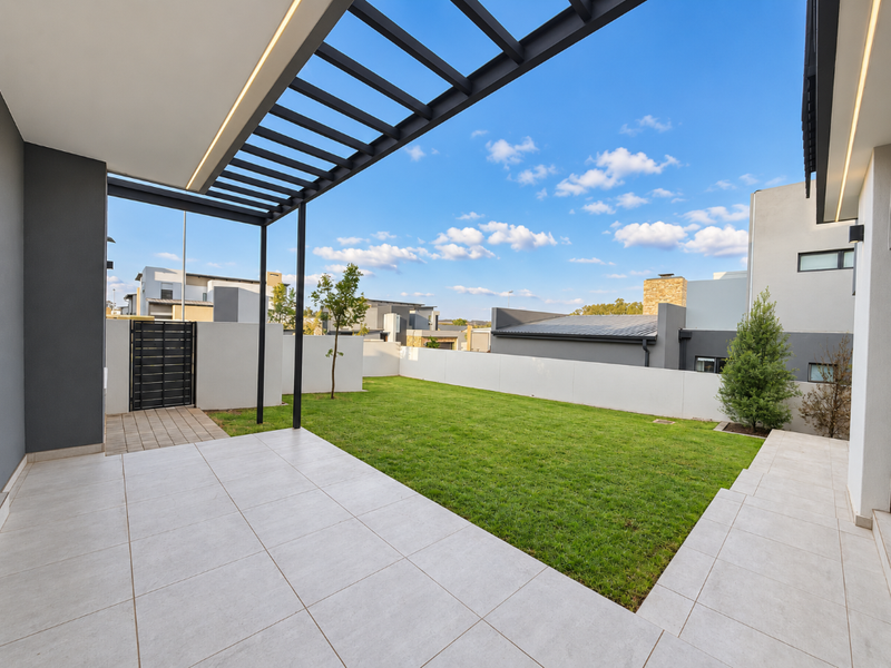 A modern covered patio featuring tiled flooring, a sleek pergola structure with integrated lighting, and a well-maintained private garden.