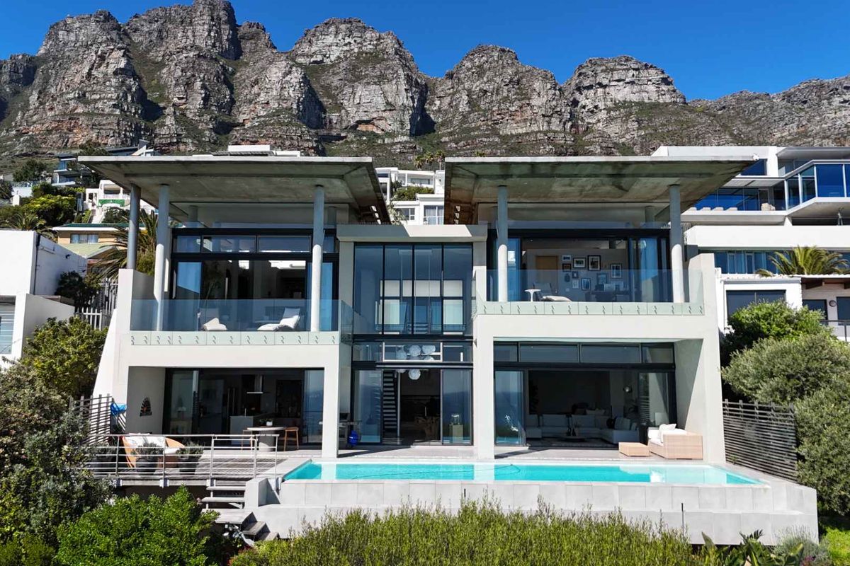 Modern multi-level architectural residence featuring a swimming pool, expansive glass facades, and concrete structural elements set against a dramatic mountain backdrop.