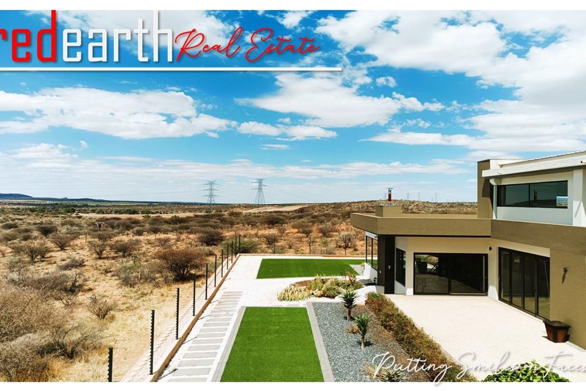 Aerial view of a modern residence featuring a landscaped rear garden, paved patio area, and expansive views of the surrounding arid landscape.
