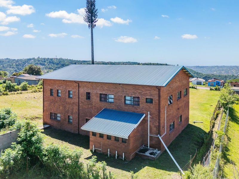 Aerial view of a two-story brick residential building featuring a metal roof and an integrated telecommunications tower on a spacious plot.