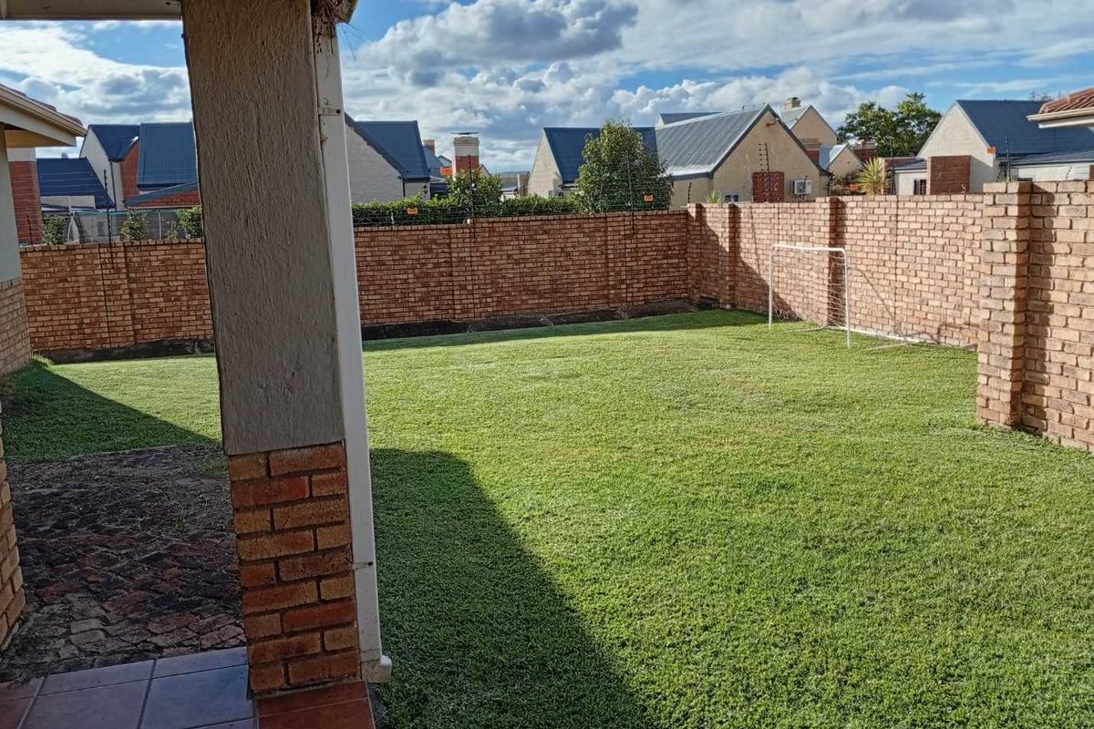 A private rear garden featuring a well-maintained lawn, enclosed by high brick boundary walls, viewed from a covered patio area.