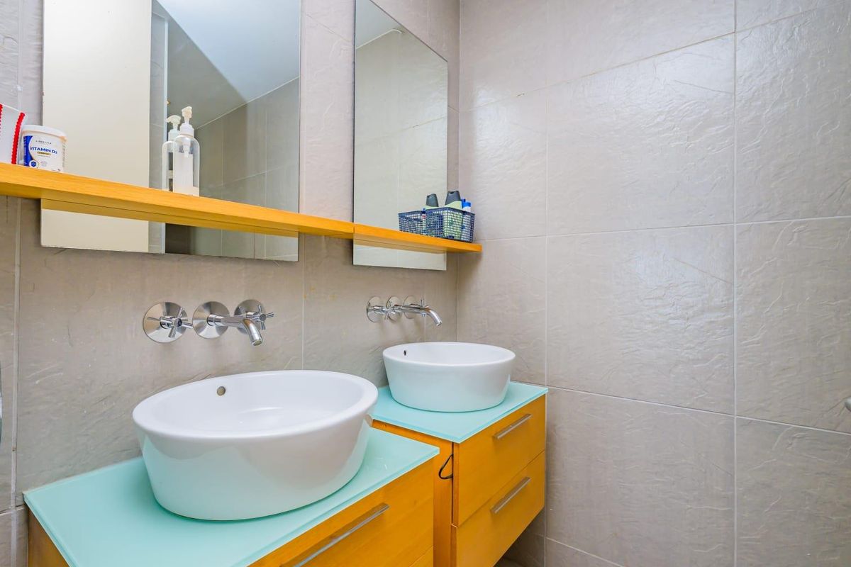 Modern bathroom featuring a double vanity with vessel sinks, wall-mounted chrome faucets, floating cabinets, and full-height wall tiling.