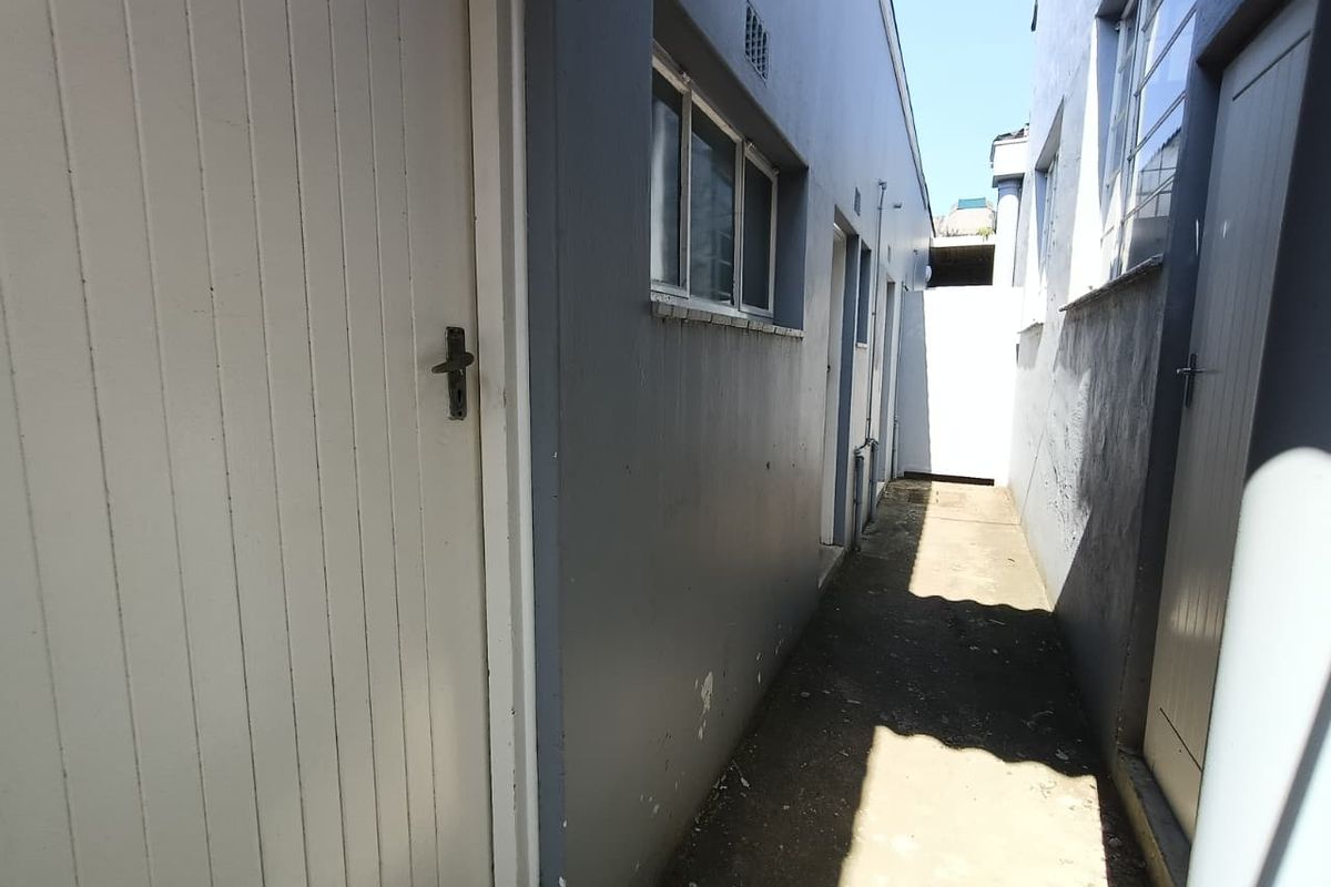 A narrow exterior side passage of an industrial property featuring concrete flooring and multiple access doors.