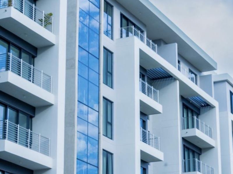 A modern apartment building facade featuring a central glass curtain wall and multiple private balconies with metal railings.