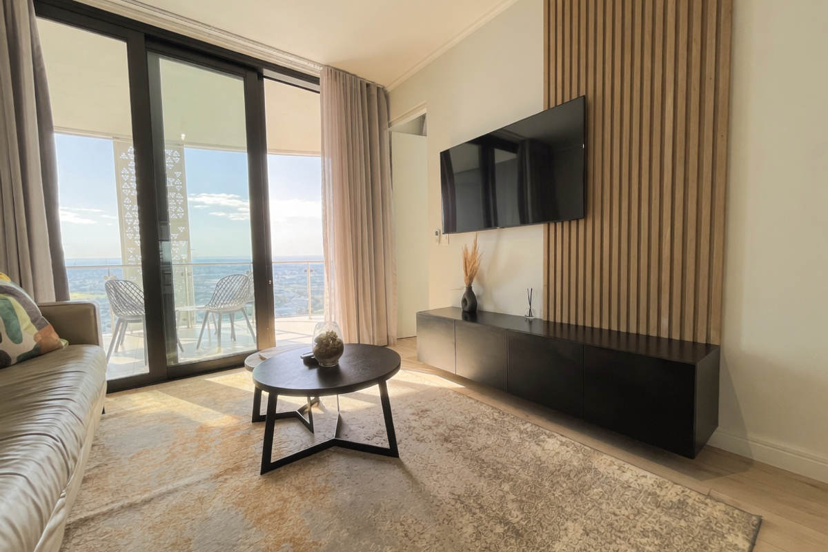 Modern living room featuring a timber slat feature wall, built-in media console, and large sliding glass doors opening to a balcony with expansive views.