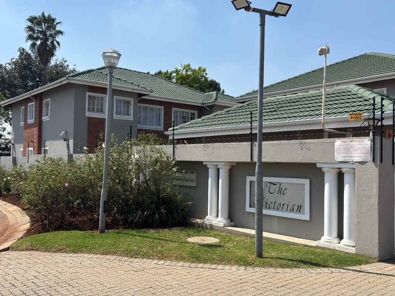 Front elevation of The Victorian cluster complex, featuring a secure gated entrance, perimeter wall with electric fencing, and well-maintained paved driveway.