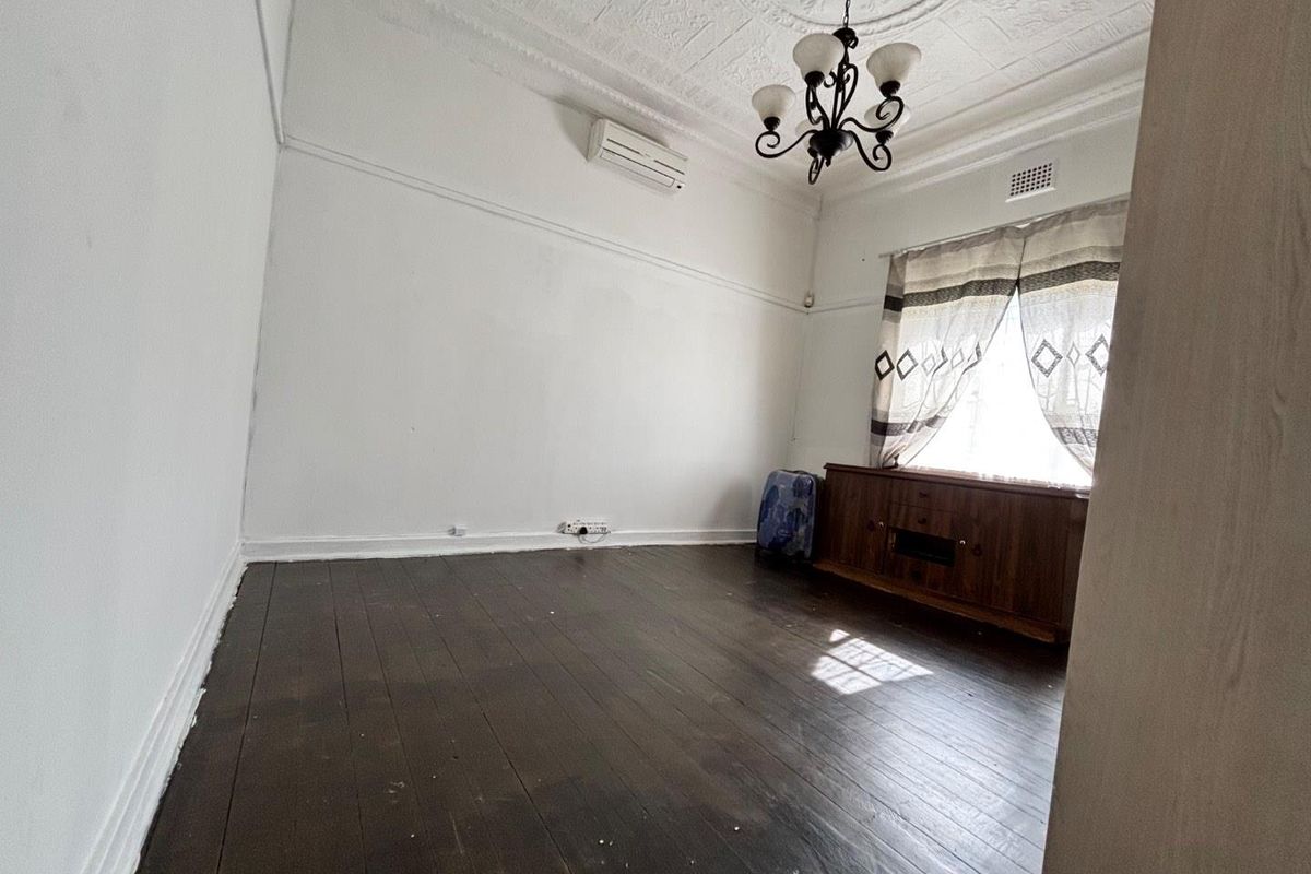 A bedroom featuring original timber flooring, ornate ceiling rose, decorative cornicing, and a wall-mounted air conditioning unit.