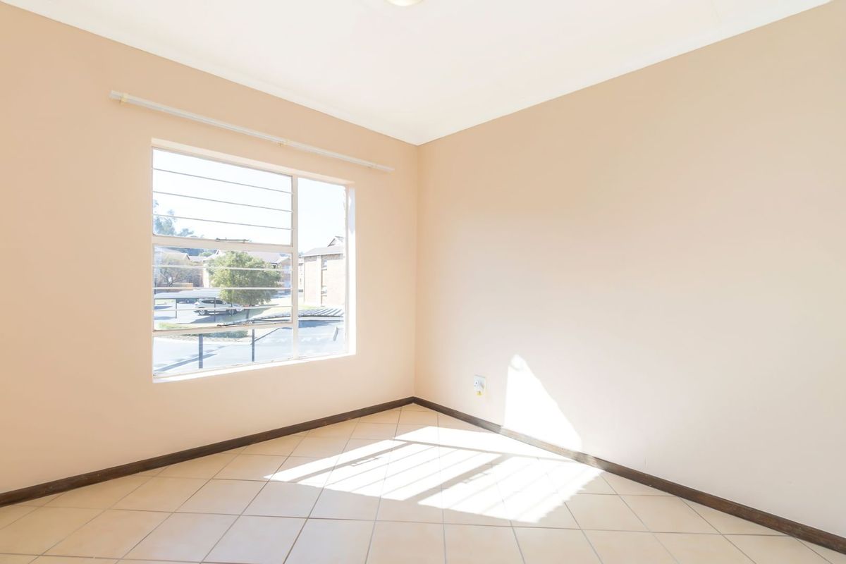 A bright, empty bedroom featuring neutral wall paint, tiled flooring, and a large window with security bars.