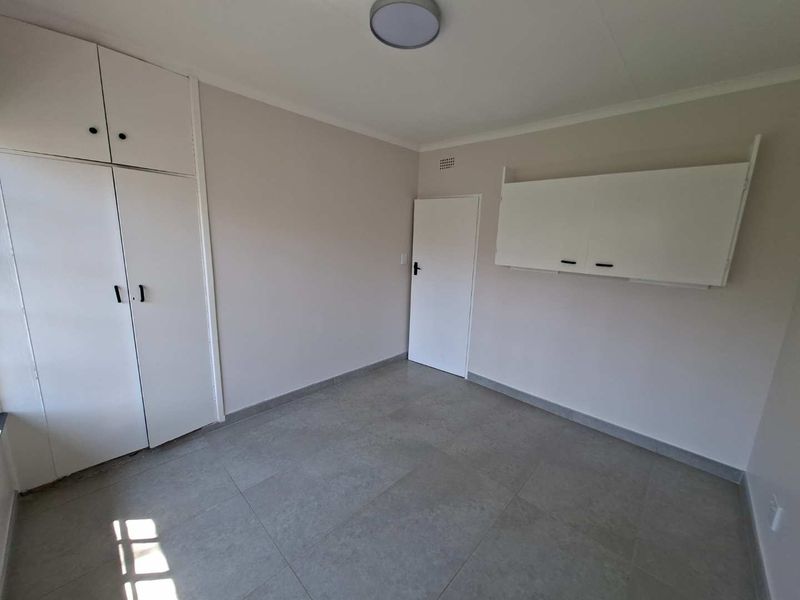A clean, empty bedroom featuring neutral walls, tiled flooring, and ample built-in storage cupboards.