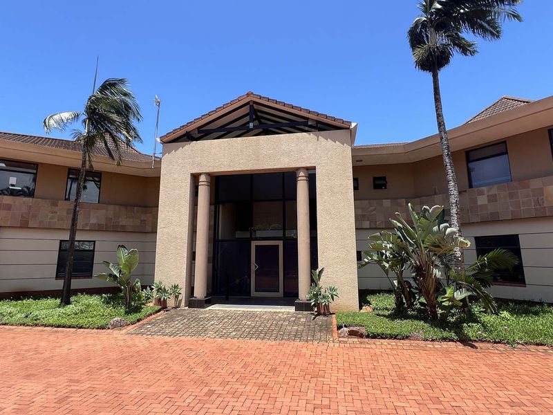 Front elevation of a professional office building featuring a paved driveway, covered entrance with columns, and well-maintained landscaped garden.