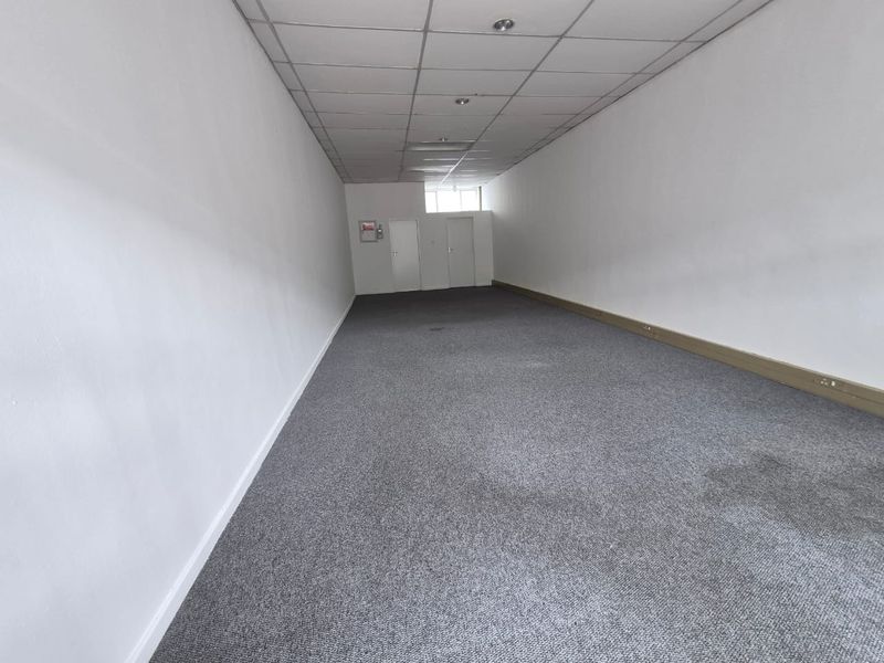 An empty, open-plan retail space featuring a suspended ceiling, recessed lighting, and grey carpet flooring, suitable for various commercial business applications.