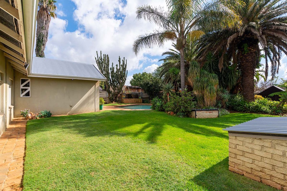 A spacious rear garden featuring a well-maintained lawn, mature palm trees, and a swimming pool area in the background.