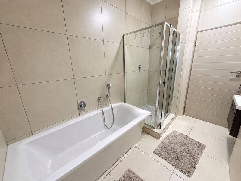 Modern bathroom featuring a freestanding bathtub, a separate glass-enclosed shower, and neutral floor-to-ceiling tiling.