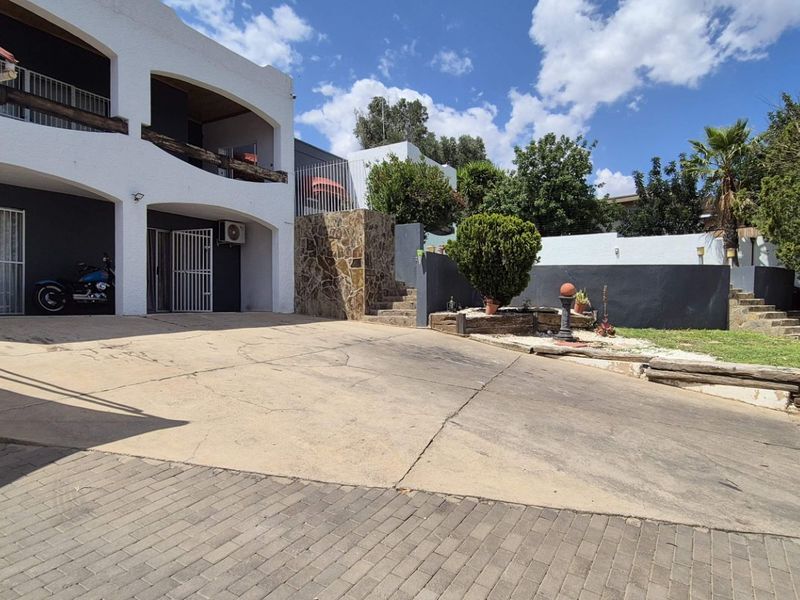 Front exterior view featuring a concrete driveway, stone-clad retaining wall, and multi-level building facade with balcony and security gates.