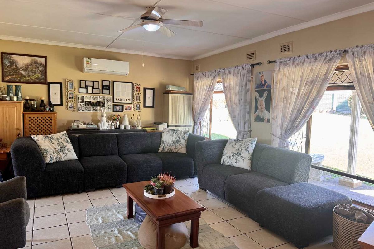 A spacious living room featuring tiled flooring, a ceiling fan, and a wall-mounted air conditioning unit, with large sliding doors providing access to the garden.