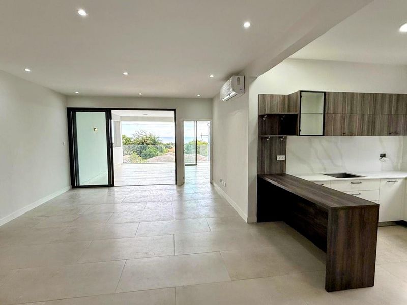 Modern open-plan living area featuring a sleek kitchen with breakfast bar, recessed lighting, and seamless access to a spacious balcony with scenic views.