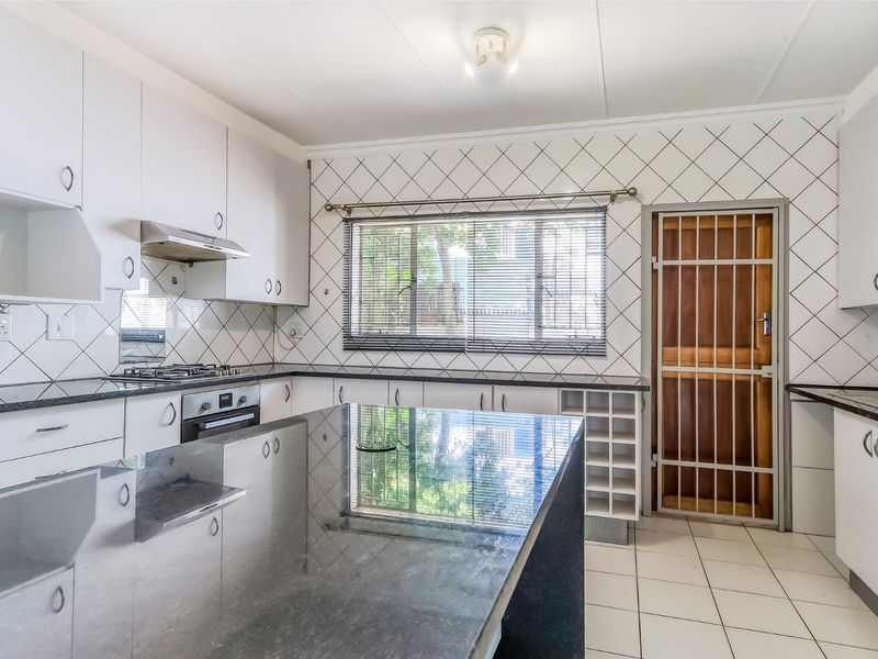 A functional kitchen featuring granite countertops, built-in oven, gas hob, and ample cabinetry, with a secure rear door and tiled flooring throughout.