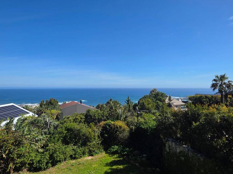 A scenic elevated view overlooking the ocean and surrounding coastal landscape, featuring a property roof equipped with solar panels.