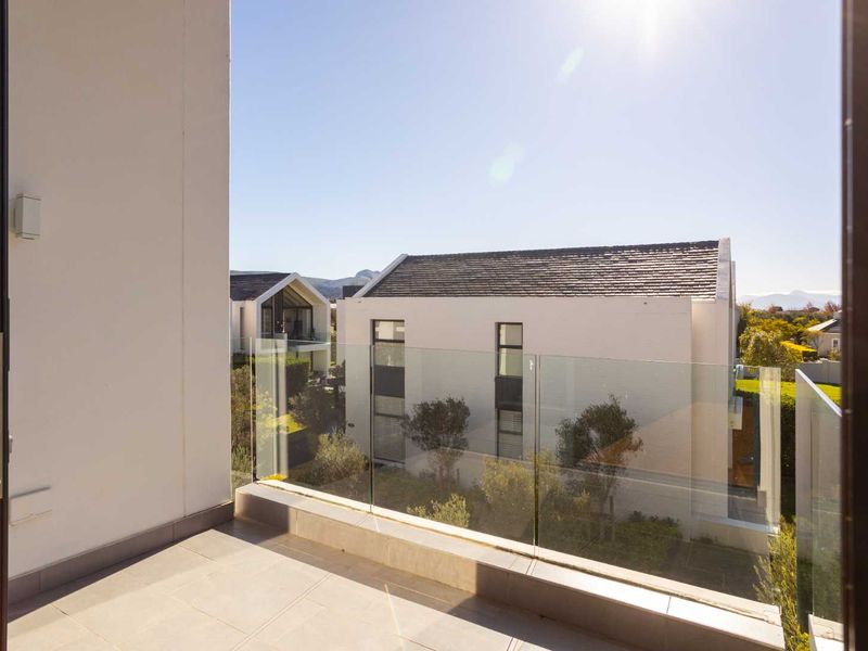 A modern balcony featuring a sleek glass balustrade and tiled flooring, offering an open view of the surrounding residential estate.