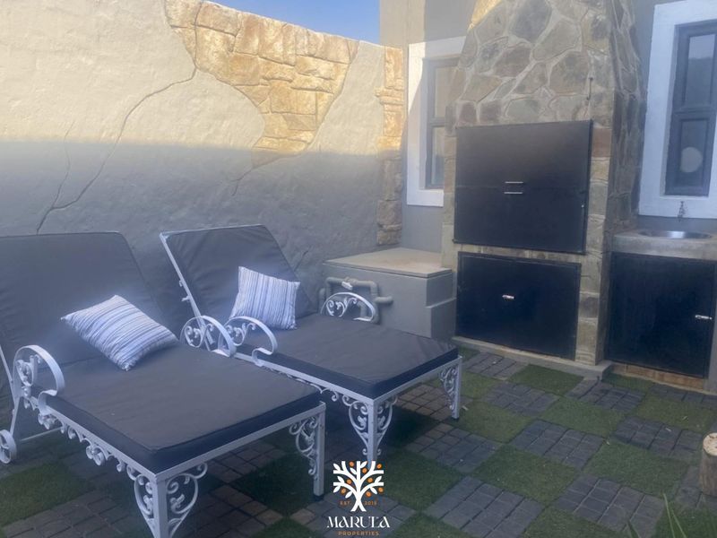 Outdoor patio area featuring a built-in braai, stone cladding, and a small integrated sink, providing a functional space for outdoor entertaining.