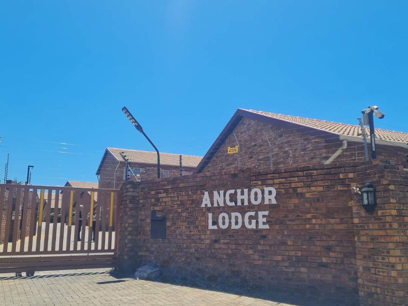 Front entrance view of Anchor Lodge featuring a brick boundary wall, security gate, electric fencing, and paved driveway access.