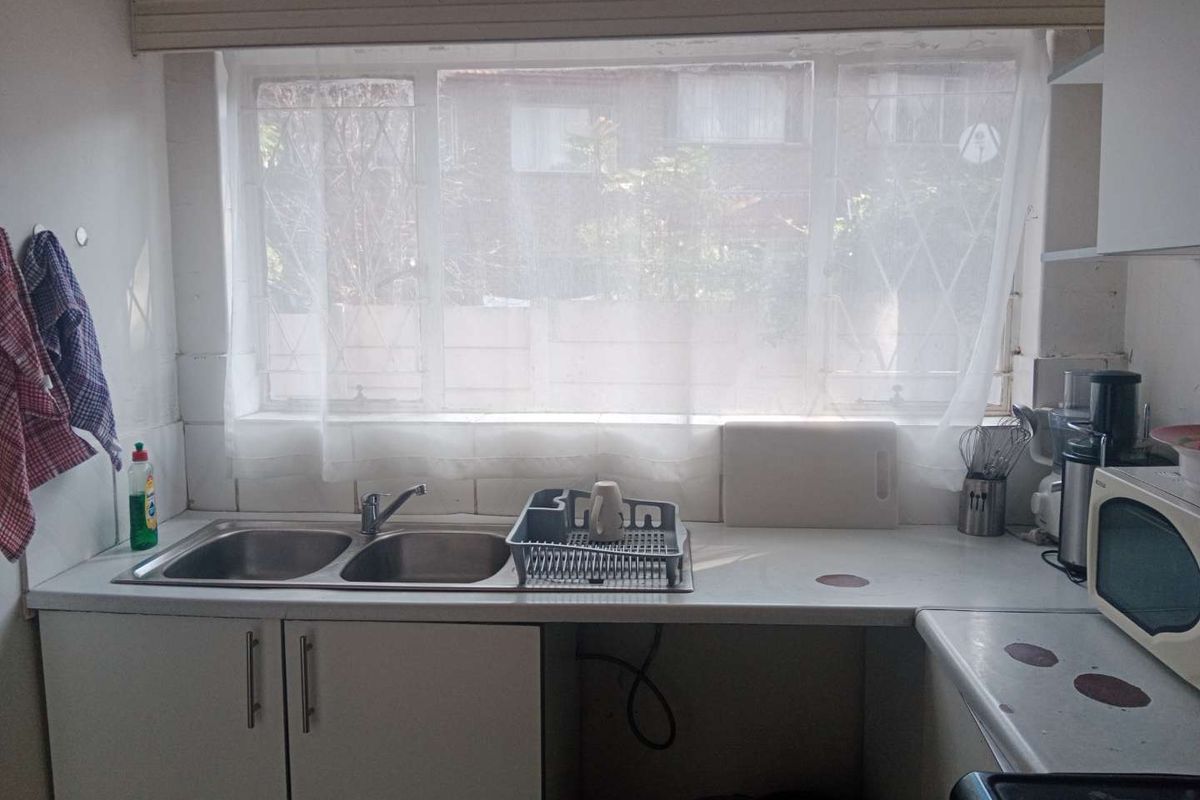 A functional kitchen area featuring a double bowl stainless steel sink, laminate countertops, and built-in base cabinetry with a tiled splashback.