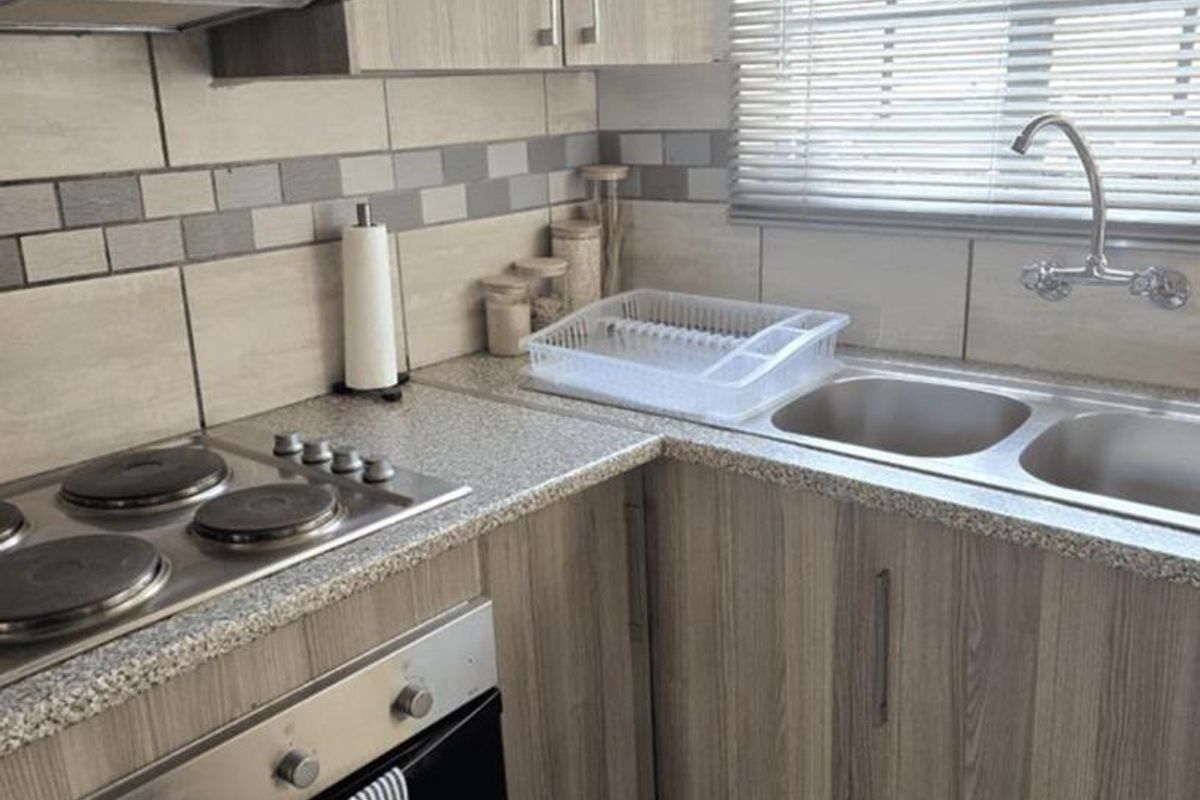 A functional kitchen featuring wood-look laminate cabinetry, granite-style countertops, a built-in oven and hob, and a stainless steel double sink with tiled backsplash.