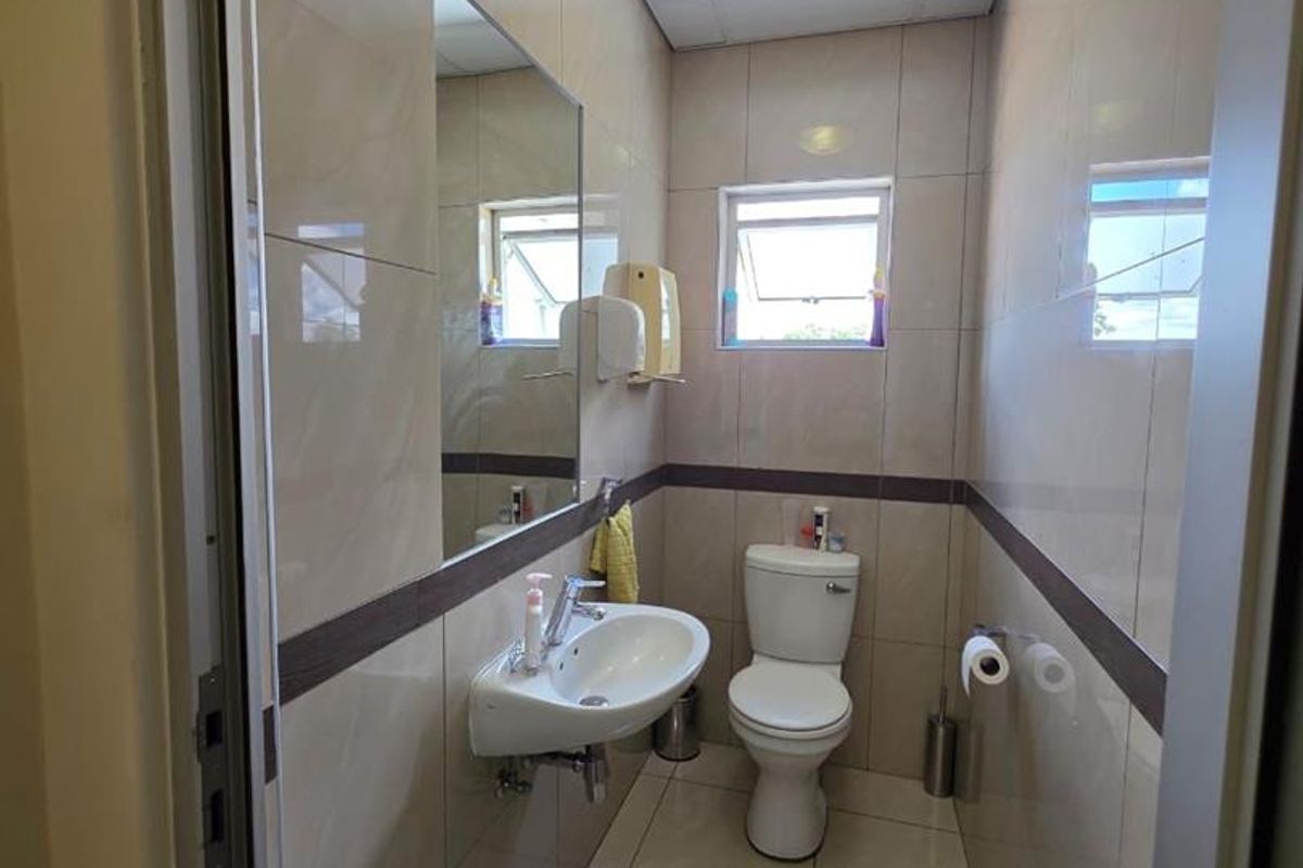 A compact, well-maintained office bathroom featuring tiled walls and flooring, a wall-mounted basin, and a standard toilet.